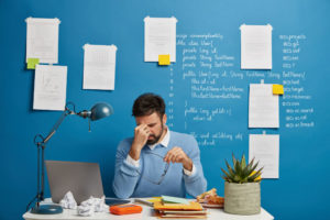 Como parar de procrastinar e tirar negócios do papel em 3 passos - Empresário exausto esfrega o nariz, tira os óculos em sua mesa de trabalho