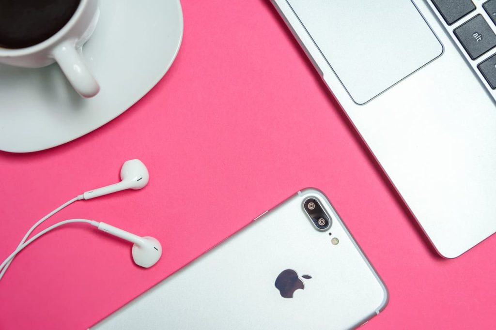 Ferramentas para Copywriters profissionais - Notebook, Celular, Fones de ouvido e xícara de café sobre uma mesa cor de rosa