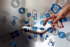 3 razões para um Social Media dominar Copywriting - Dedo tocando a tela de um celular de onde saem vários ícones de redes sociais