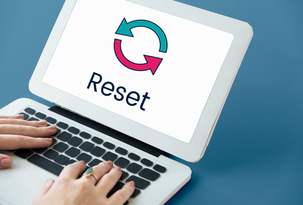 Como Copywriters de sucesso lidam com o fracasso - Mãos sobre o teclado de um notebook branco com uma imagem na tela escrito "Reset"