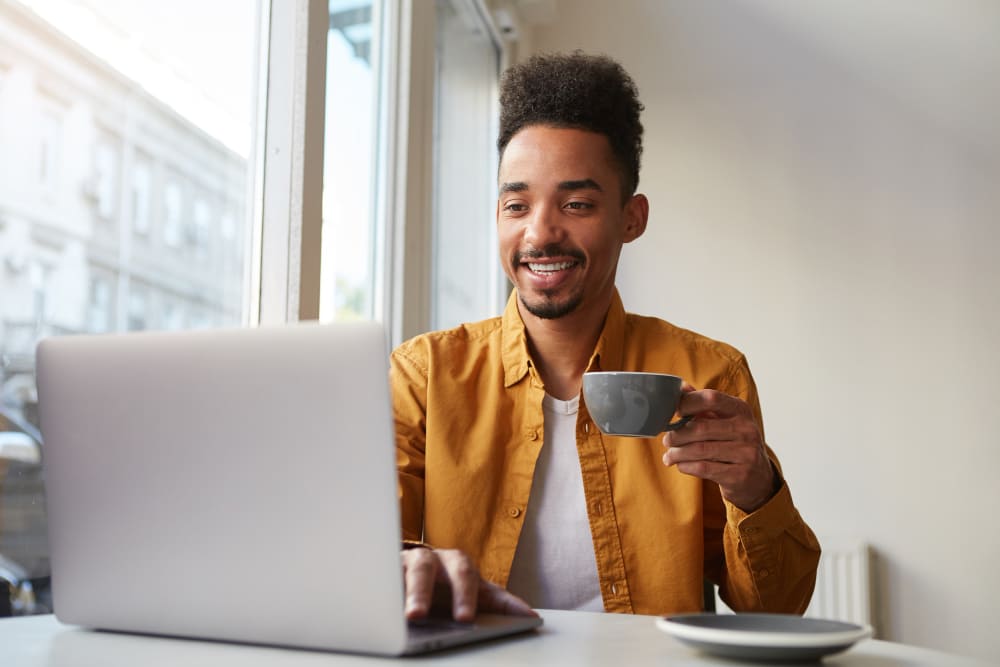 Como revisar uma página de vendas - Homem negro sorrindo com uma xícara de café na mão, sentado em frente ao seu notebook.