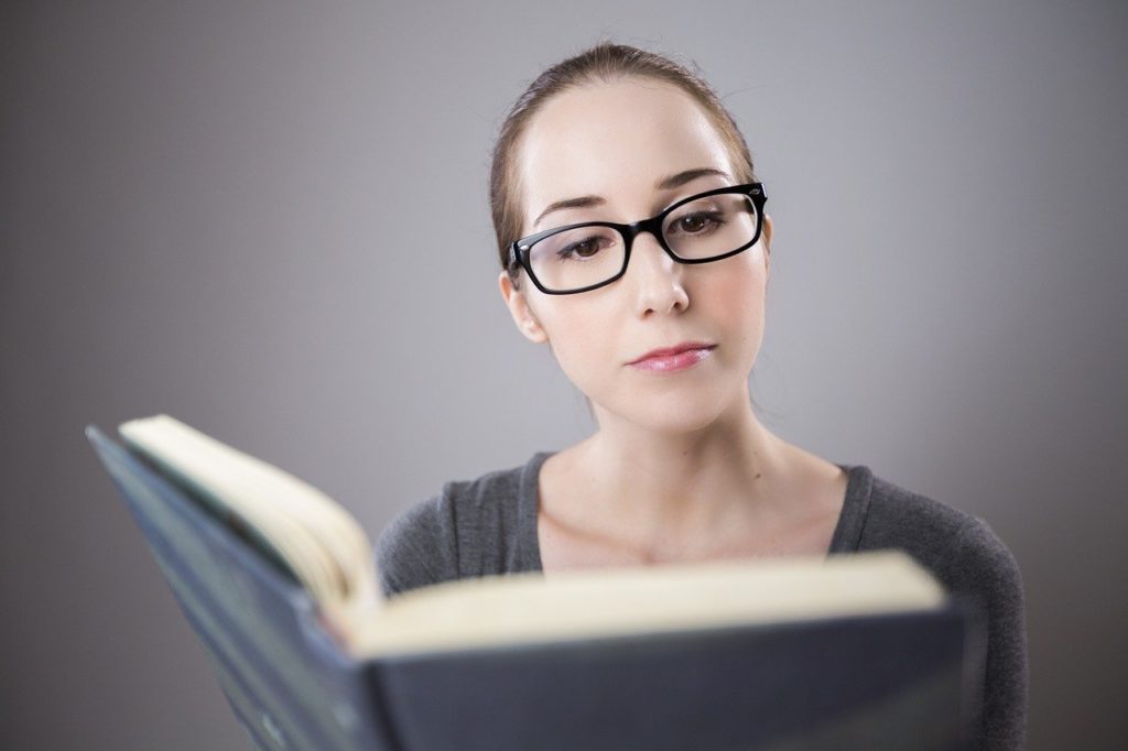 10 livros que todo Copywriter deveria ler - Mulher com óculos preto lendo um livro, em um fundo cinza.