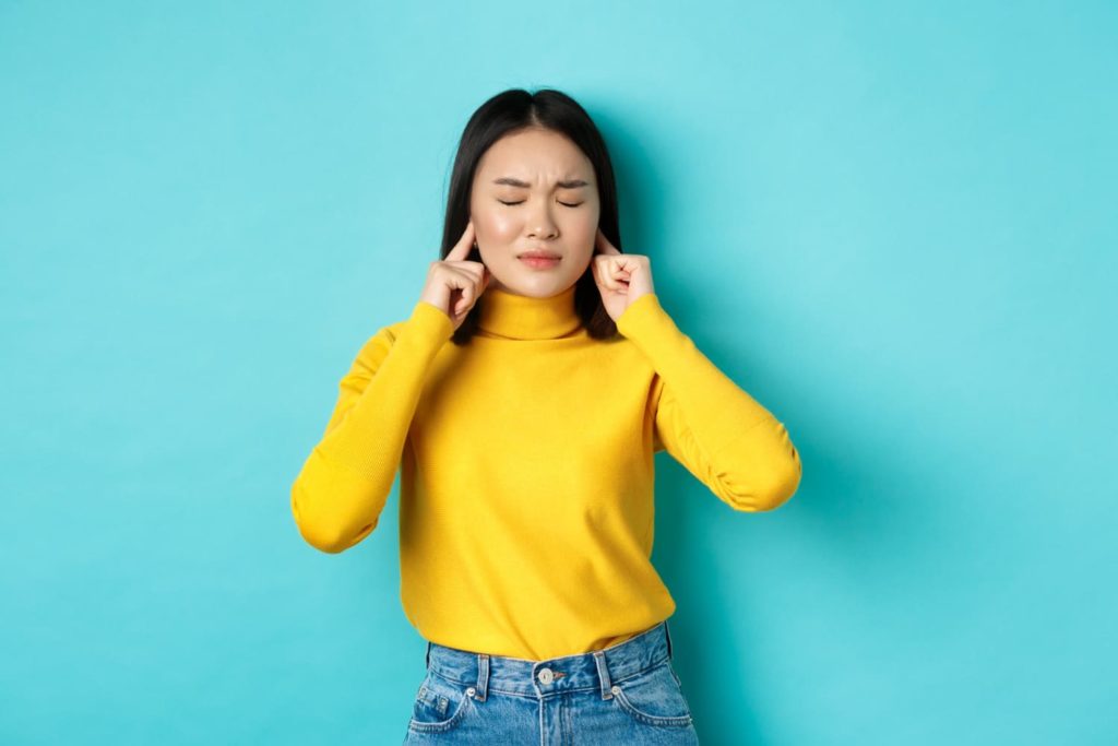 7 mitos sobre Copywriting que te impedem de lucrar com textos - Jovem asiática, vestida com uma blusa amarela, tapando os ouvidos.