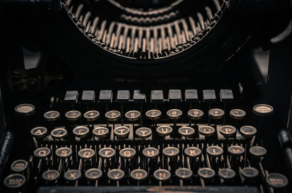 A diferença entre o escritor milionário e os escritores geniais que morreram pobres - Imagem de uma máquina de escrever preta com teclas na cor bronze