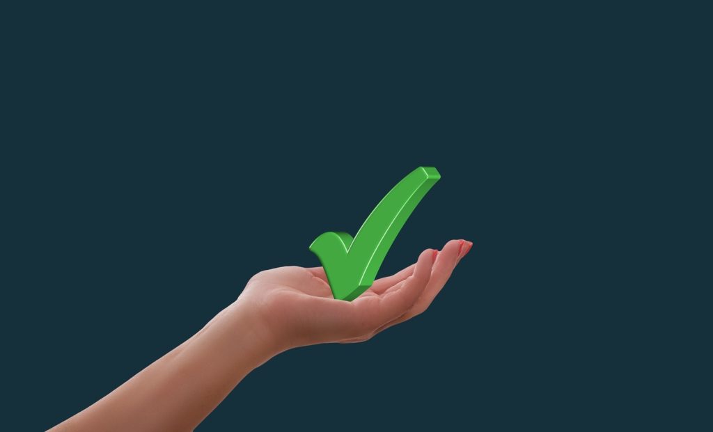 5 elementos de persuasão obrigatórios em Copy para anúncios - Mão segurando um ícone de check na cor verde