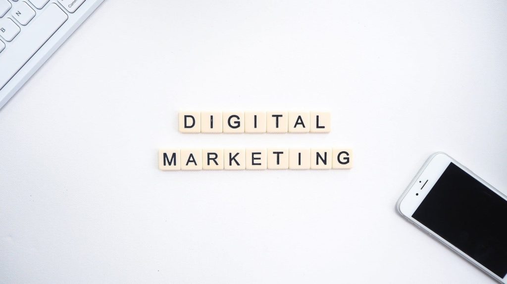 O que são produtos digitais e como fazer dinheiro online com eles - Notebook e celular sobre uma mesa branca com peças formando a palavra Digital Marketing