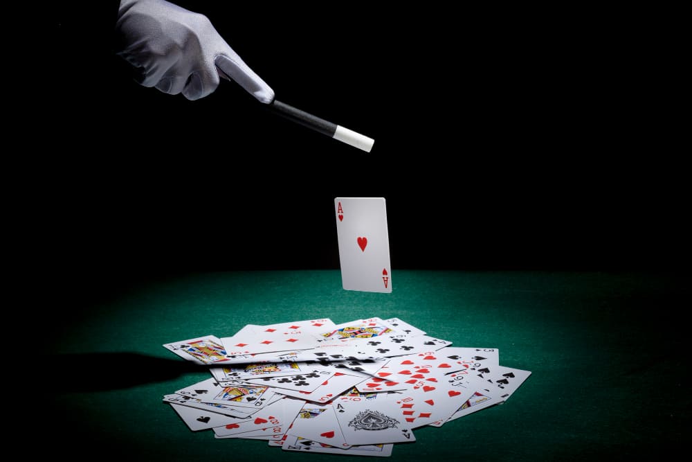 3 falhas no mercado de trabalho tradicional que te afastam da abundância financeira - Mão de um mágico fazendo truques com cartas, sobre um fundo escuro.