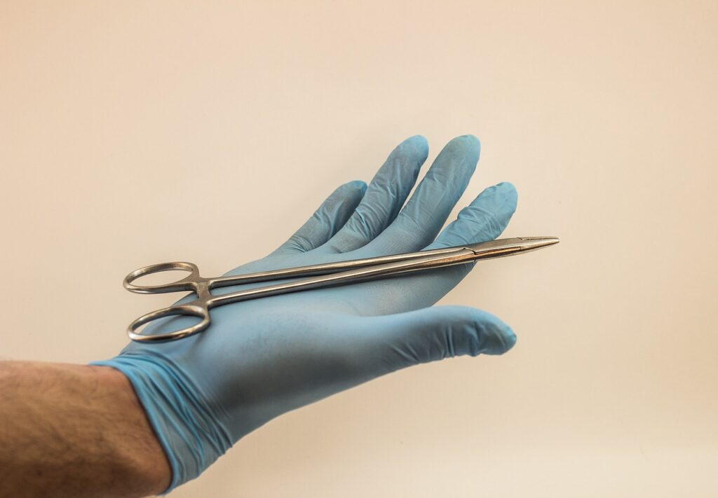 Como começar no Copy - O cirurgião da comunicação - Mão com uma luva azul, segurando uma tesoura cirúrgica